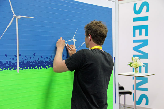 Artists from Berlin-based KlebeBande created windpower-inspired tape art at the Siemens booth yesterday and today, attracting many admirers. According to Siemens, the tape art helps demonstrate the company’s “strong bond” to American wind power.